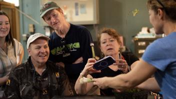 Visitors gathered around a table, closely examining and taking photos of a plant held by an instructor.
