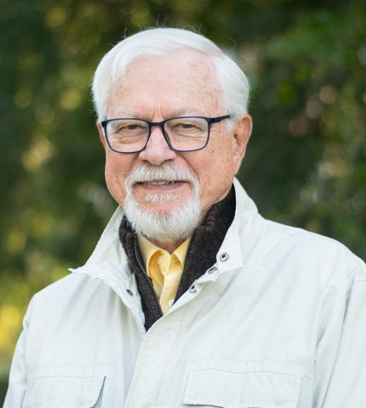 A man with white hair standing outside.