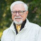 A man with white hair standing outside.