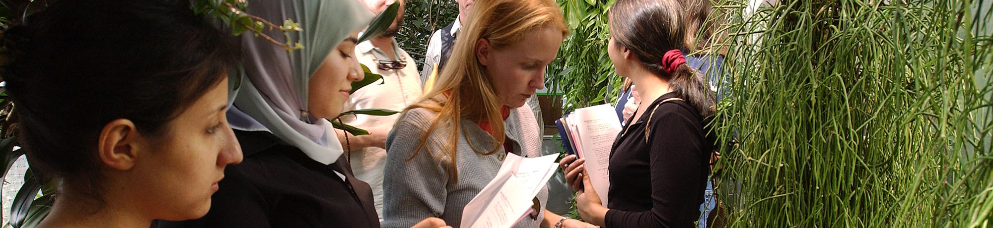 A grou pof people in various types of attire holding clipboards and taking notes in a greenhouse setting.